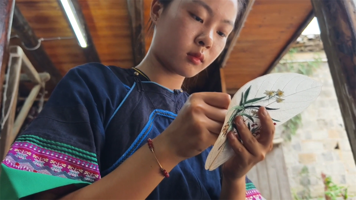 Yang Li's apprentice embroiders orchids on a piece of leaf-vein at a workshop in Tongren City, Guizhou Province. /Photo provided to CGTN