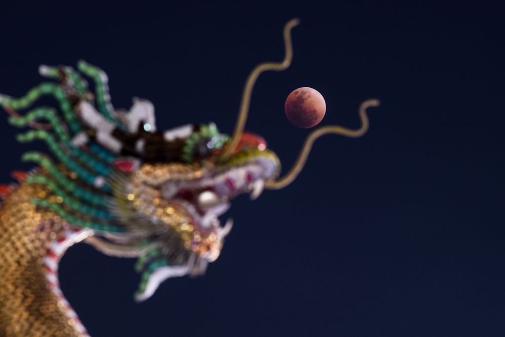 The moon is seen rising over the horizon above the head of a dragon statue at a Buddhist temple in Bangkok. /CFP