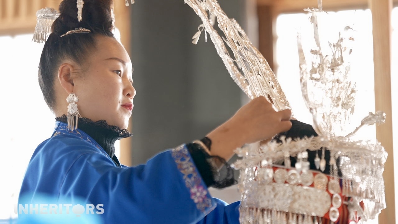 A Miao woman helps her sister to put on some silver. /CGTN