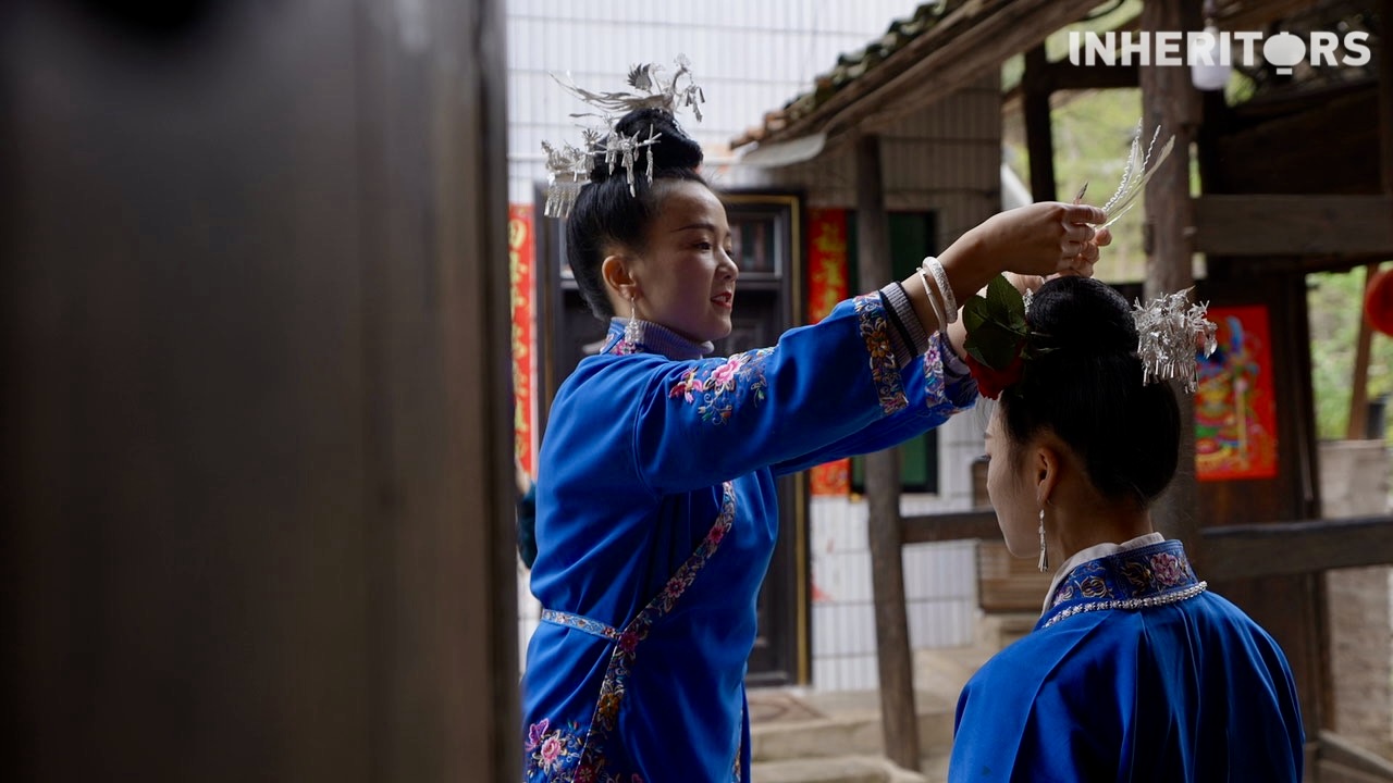 A Miao woman helps her sister to put on some silver. /CGTN