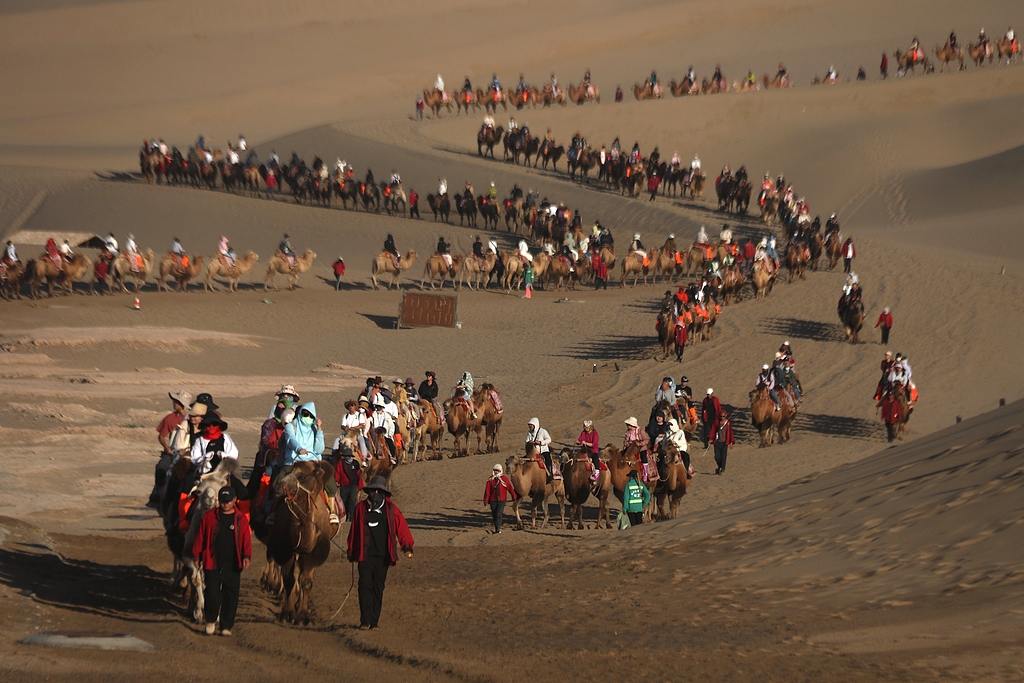 Visitors enjoy the fun of camel riding at the Mingsha Mountain and Crescent Spring scenic spot in Dunhuang, Gansu Province, September 17, 2024. /CFP