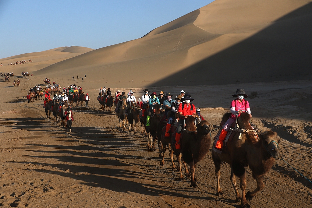 Visitors enjoy the fun of camel riding at the Mingsha Mountain and Crescent Spring scenic spot in Dunhuang, Gansu Province, September 17, 2024. /CFP