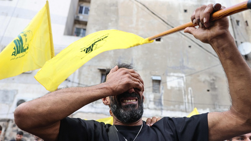 Seorang pria bereaksi sambil memegang bendera Hizbullah selama pemakaman orang-orang yang tewas setelah ratusan alat pemanggil meledak dalam gelombang mematikan di Lebanon pada hari sebelumnya, di distrik Beirut selatan, 18 September 2024. /CFP