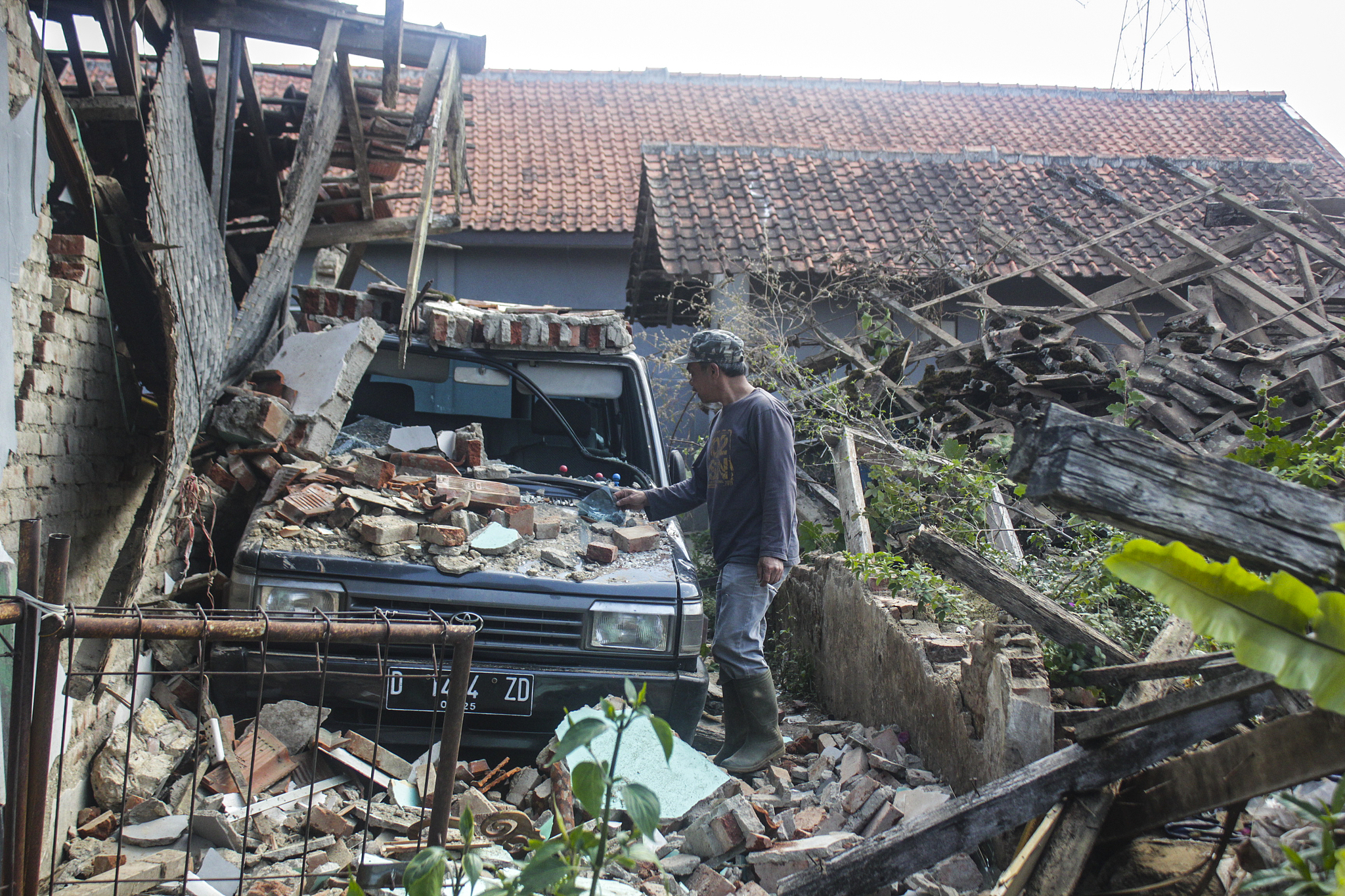 A resident cleans a car that was badly damaged by the rubble of a house after a magnitude-5 earthquake hit Cibereum Village, Bandung Regency, West Java, Indonesia, September 18, 2024. /CFP