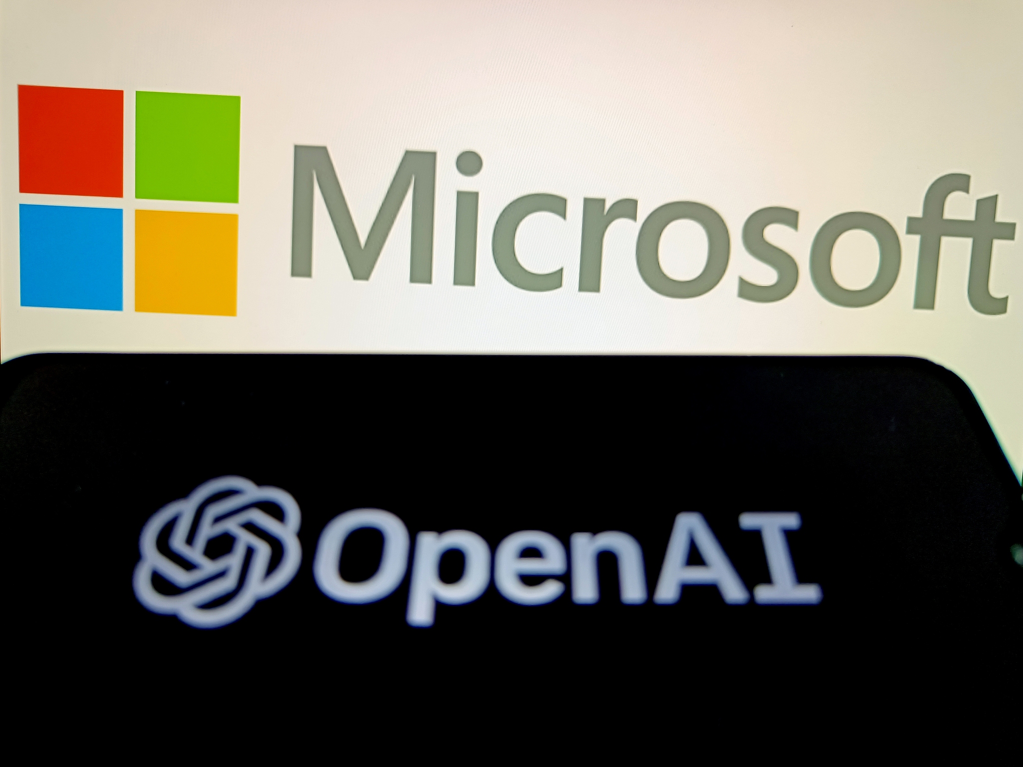 A smartphone displays OpenAI logo with the Microsoft logo visible in the background. /CFP
