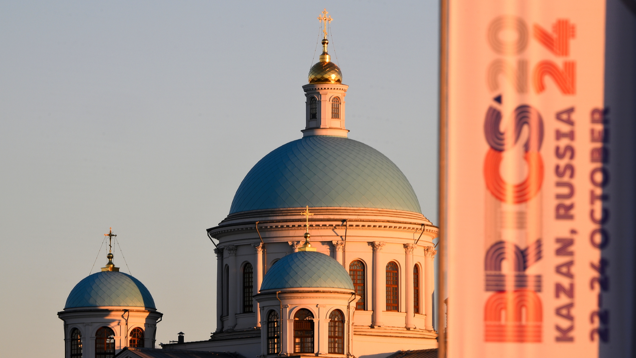 Sunlight shines on a banner with the upcoming 16th BRICS Summit logo and the Cathedral of the Icon of the Our Lady of Kazan in the background in Kazan, Russia, October 14, 2024. /CFP