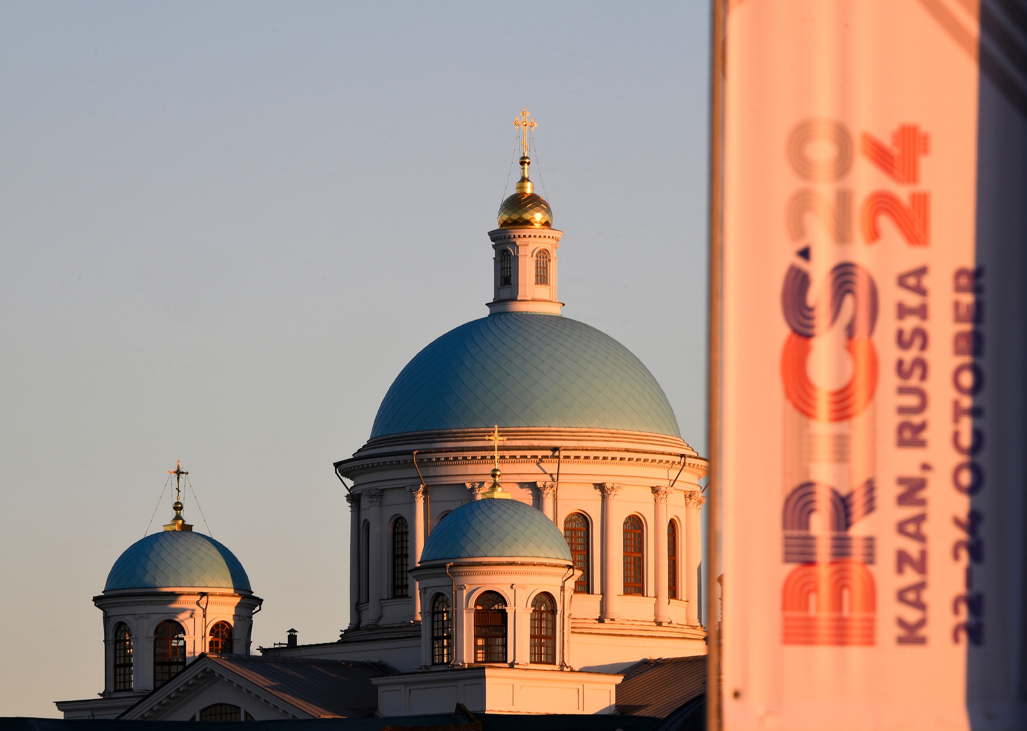 Sunlight illuminates a banner featuring the logo of the 16th BRICS Summit, with the Cathedral of Our Lady of Kazan in the background, Kazan, Russia, October 14, 2024. /CFP