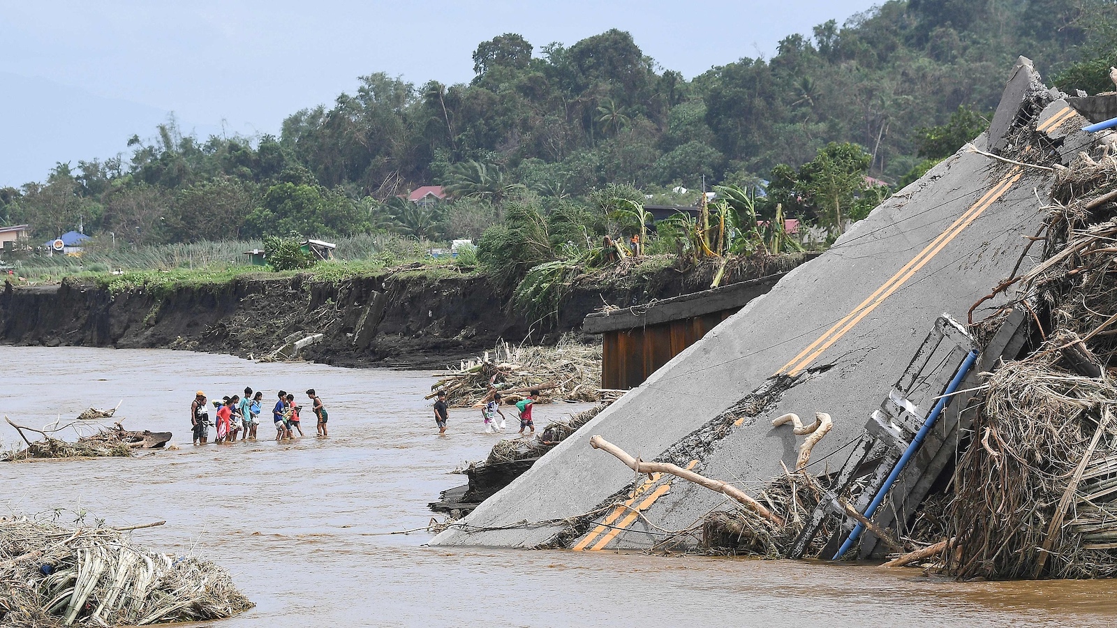 People cross a river next to a bridge that collapsed in rains brought about by Tropical Storm Trami, in Laurel, Batangas province, south of Manila, the Philippines, October 25, 2024. /CFP