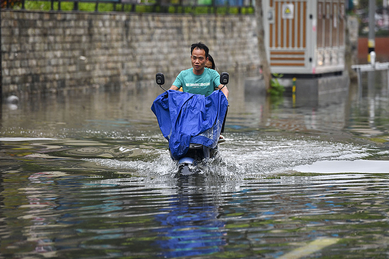 Residents ride an electric scooter through floodwaters on a road in Haikou City, Hainan Province, south China, October 30, 2024. /CFP