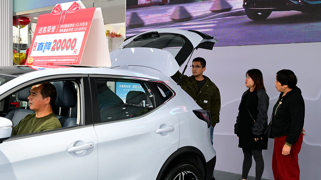 A consumer is test-driving a car at an auto show, with a promotional sign on top of the car displaying 