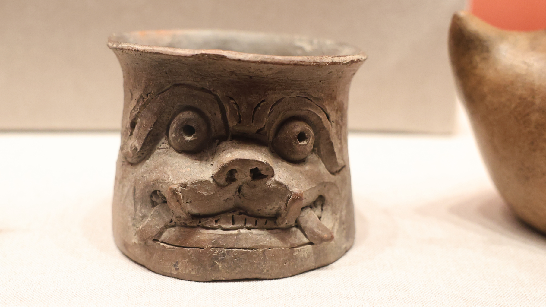 A cylindrical ceramic bowl with a human face is on display at 