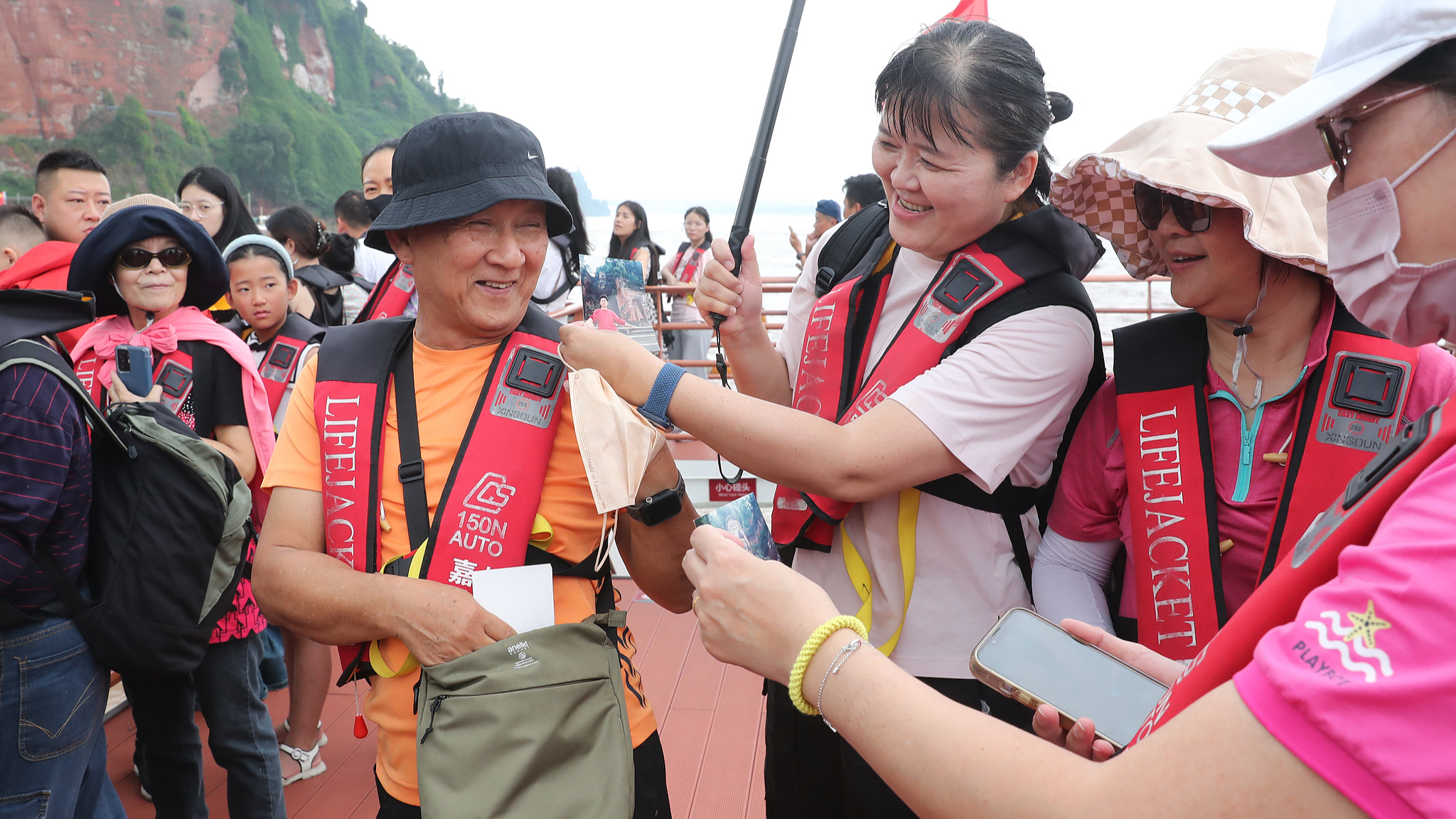 A tourist from southeast China's Taiwan region shows other visitors a photo taken 30 years ago of himself posing with the Leshan Giant Buddha statue at the Leshan Giant Buddha scenic area in southwest China's Sichuan Province, September 14, 2024. /CFP
