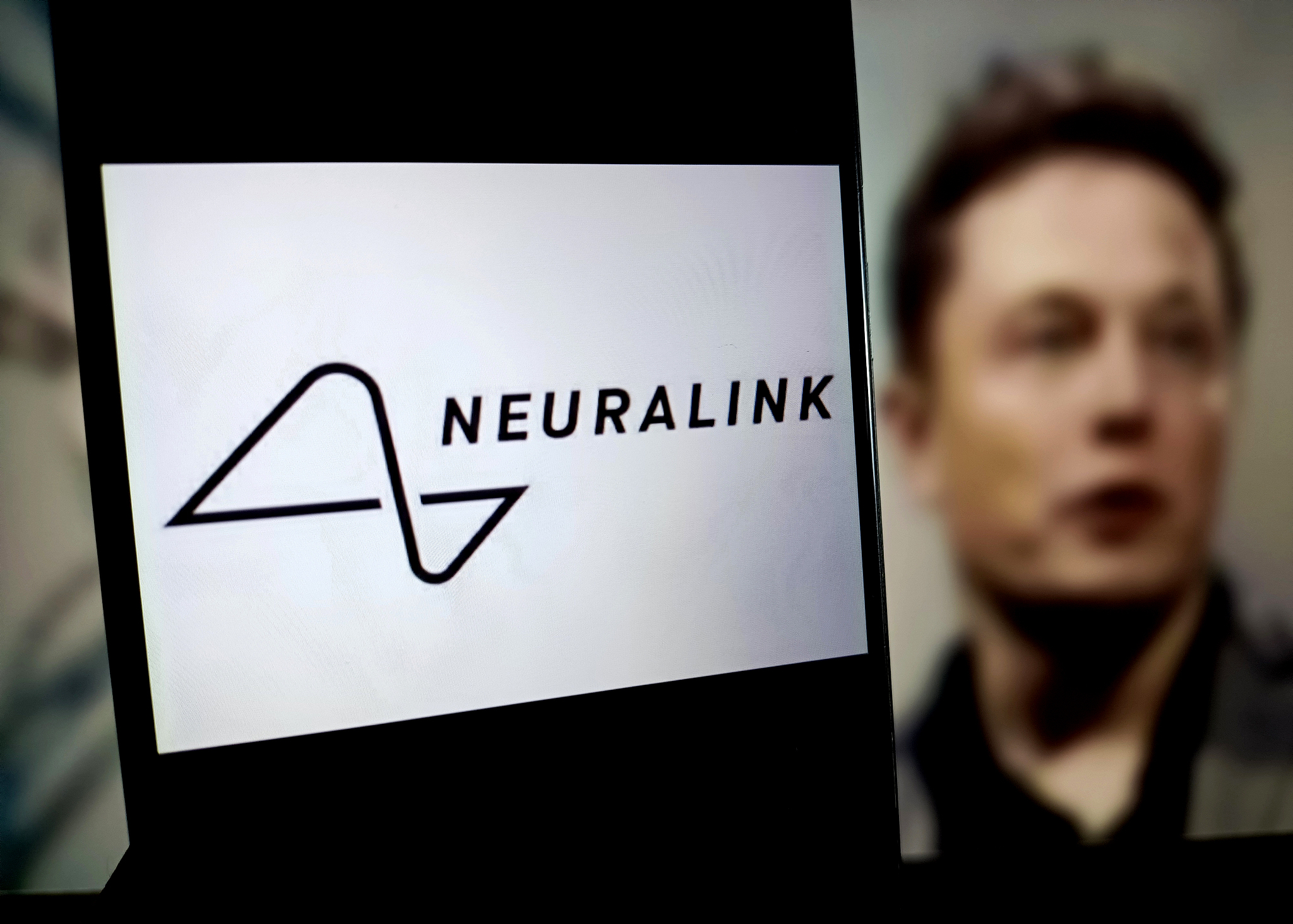 The Neuralink logo displayed on a mobile screen with founder Elon Musk seen in the background. /CFP