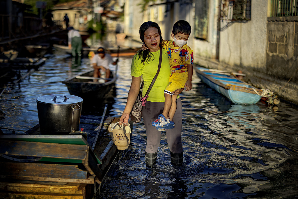 A resident carries a child as she wades through floodwater in Dela Paz village, which has remained flooded since Tropical Storm Trami hit a month ago and was hit again by Typhoon Man-yi this week. Binan, Laguna Province, Philippines. November 20, 2024. /CFP