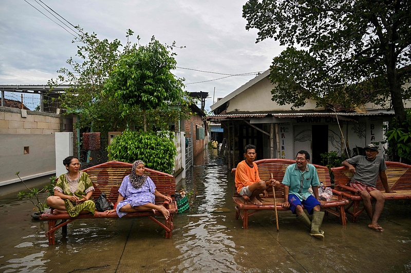 Residents sit on benches amid floodwaters from an overflowing river following torrential rain in Tempuran village in Mojokerto, East Java province on December 9, 2024. /CFP