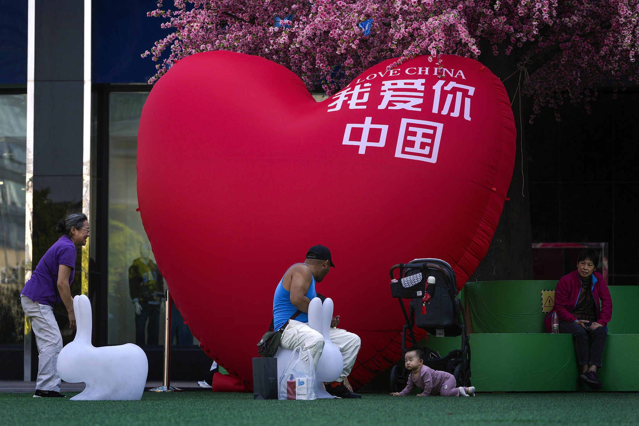 People cheer a toddler near a giant heart-shaped decoration outside a shopping mall in Beijing, September 23, 2024. /CFP