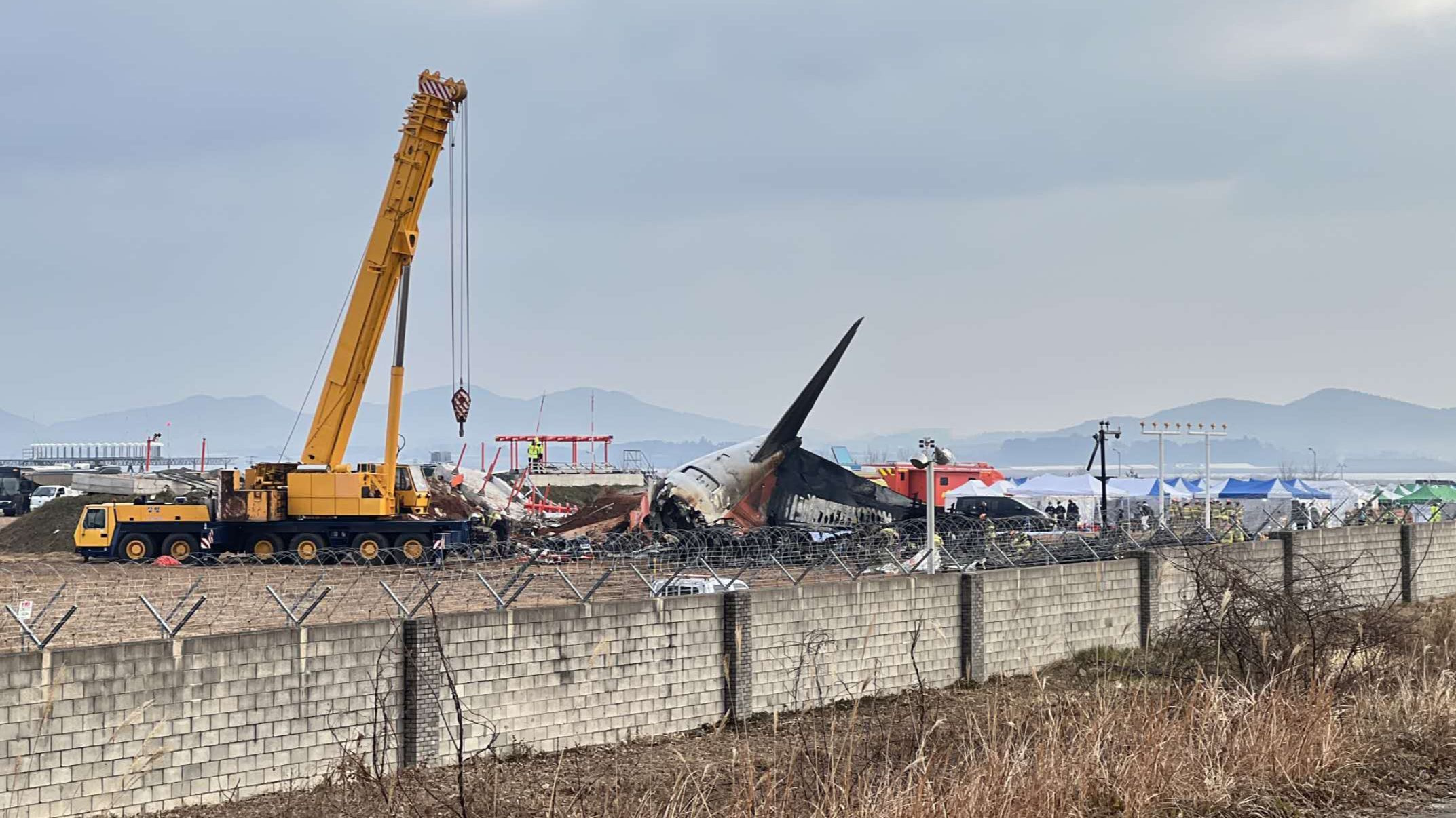 A giant yellow crane lifts the burned-out fuselage of the orange-and-white aircraft on the runway at Muan International Airport in Muan, South Korea, December 30, 2024. Shane Hahm/CGTN