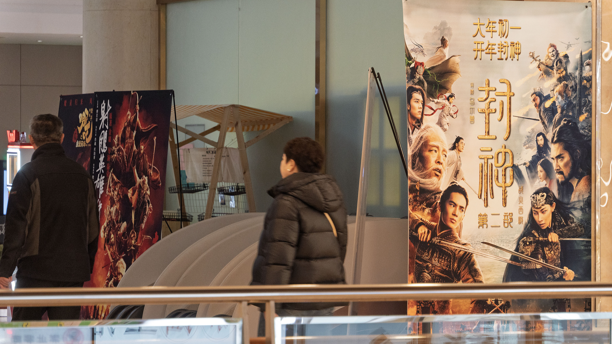 People pass by a display board of new films for the 2025 Spring Festival at a cinema hall in Nanjing City, east China