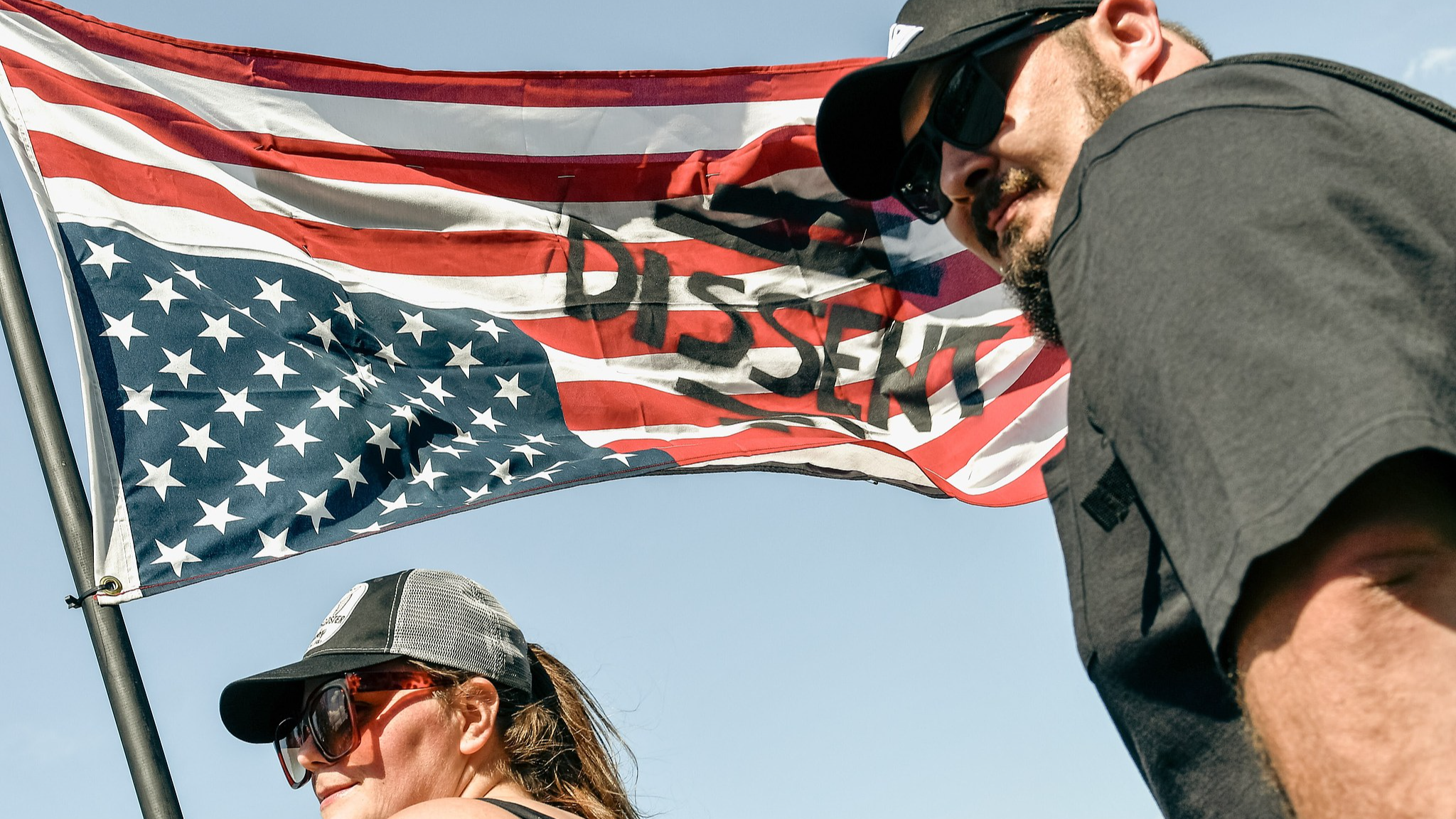 A protester waves an inverted American flag with the words 'I Dissent' alongside approximately 3,000 others, showing their displeasure with President Trump's policies outside Macomb Community College in Warren, Michigan, U.S., April 29, 2025. /VCG
