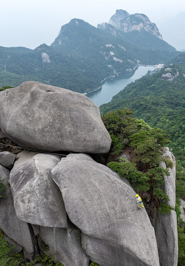 Tu Yousheng picks up trash along the cliffs of Tianzhu Mountain in Anqing, Anhui Province, China, on May 18, 2025. /VCG