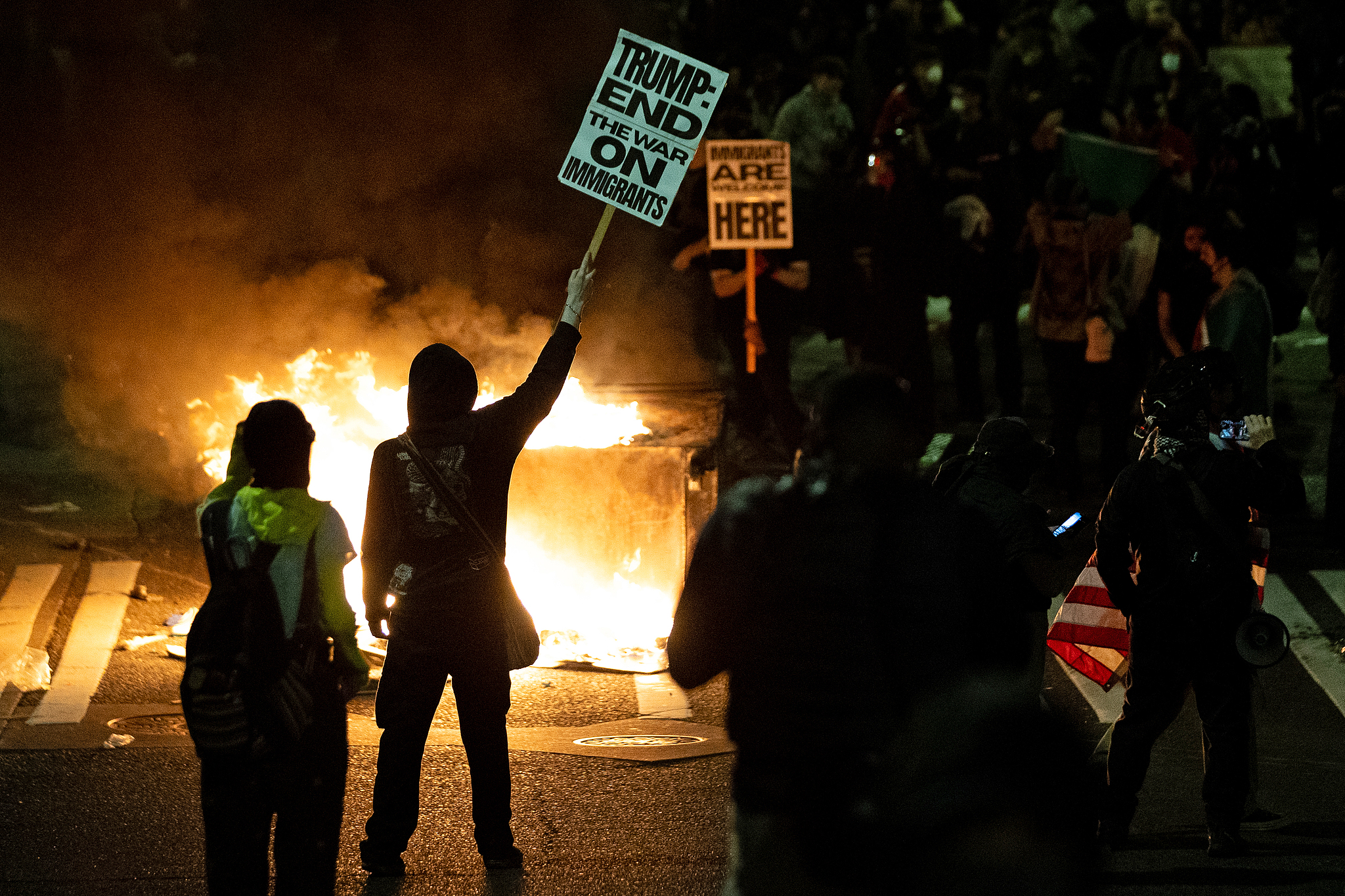 A protestor lifts a sign in front of a dumpster that was set on fire during a protest against federal immigration arrests in Seattle, Washington, the U.S., June 11, 2025. /VCG