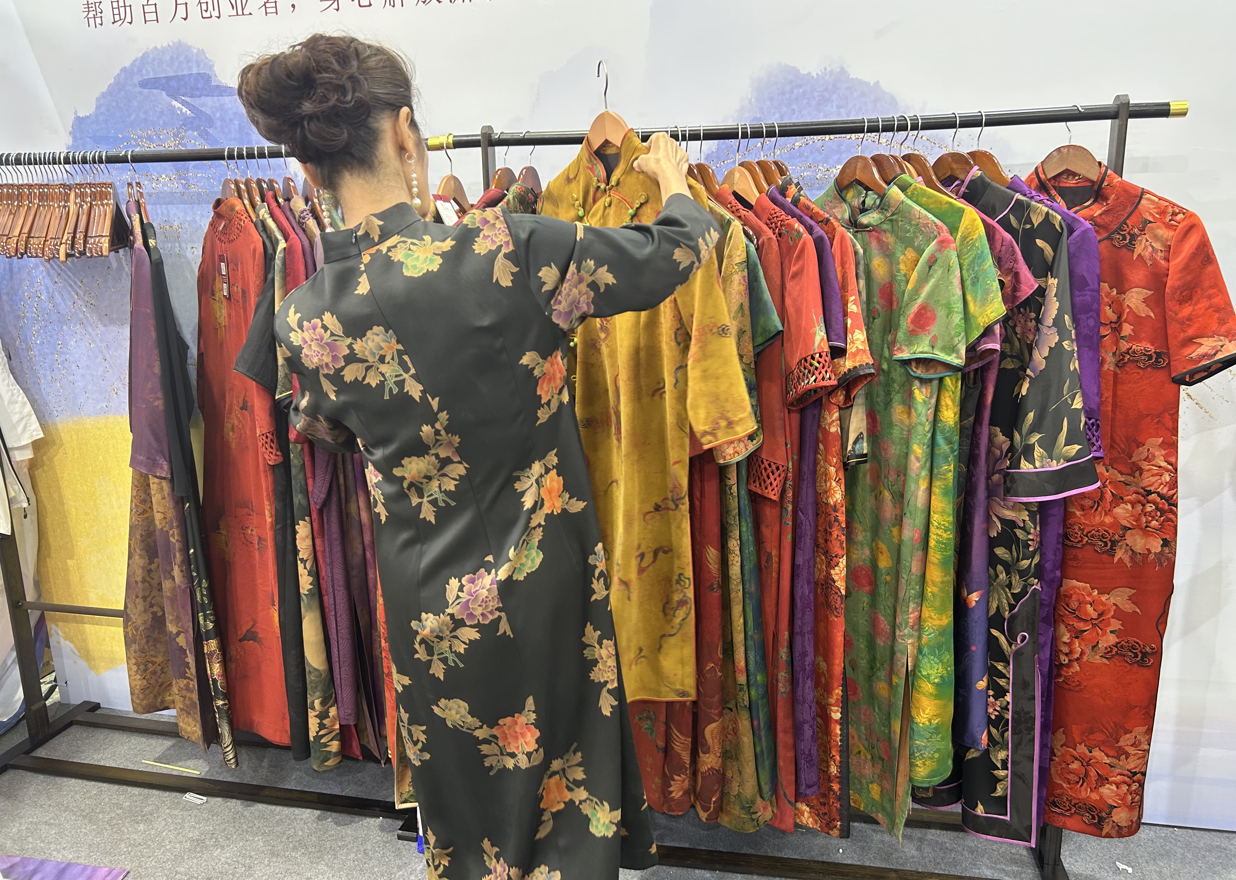 A woman chooses a qipao garment made of Xiangyunsha, the world's only silk fabric dyed exclusively with natural plant-based dyes, at the Beijing International Tea Trade Expo 2025 held in early July. /CGTN