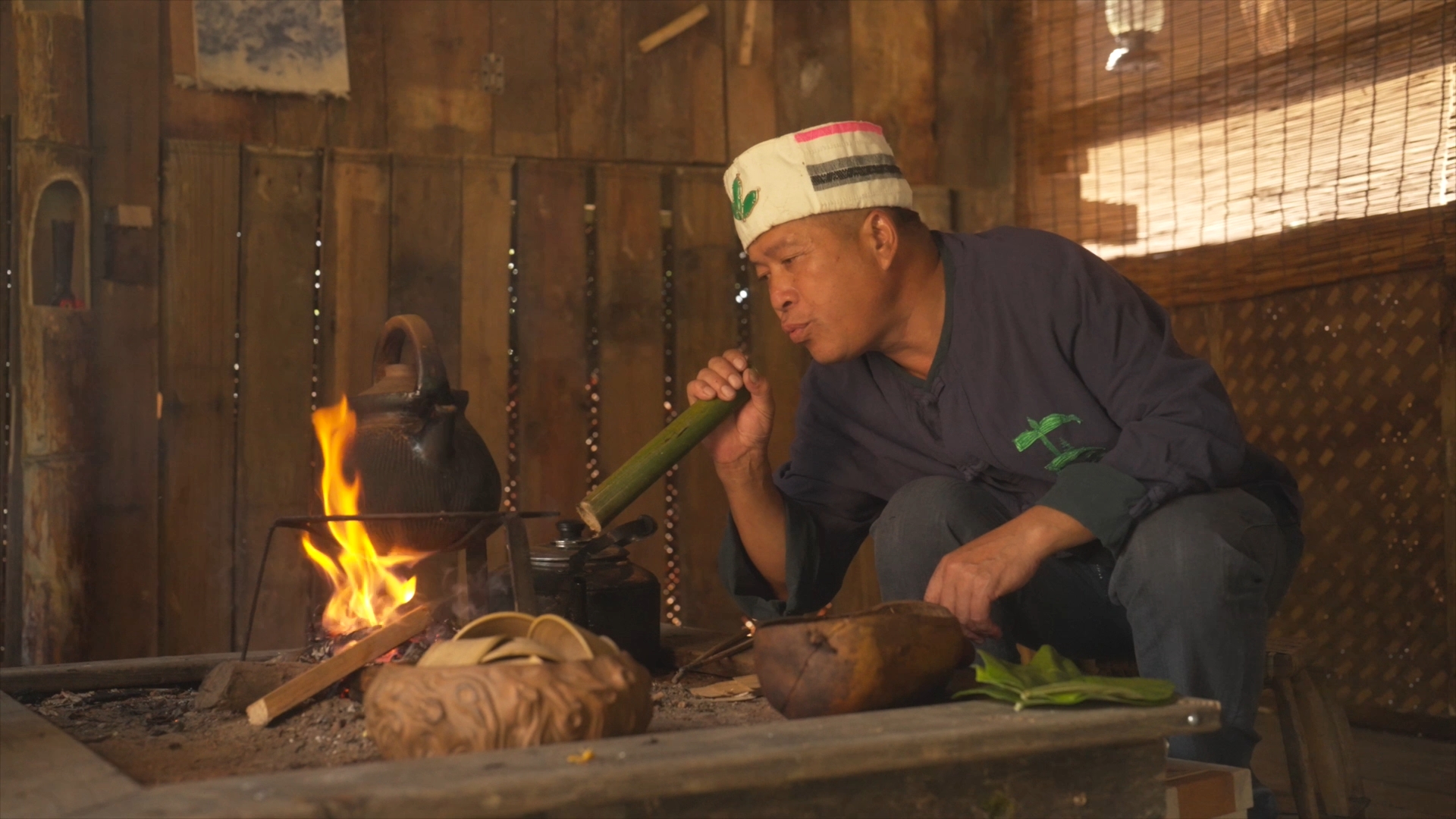 A man of the Blang ethnic group blows air into the fire with a bamboo tube to keep it burning strong for tea preparation, Pu'er City, southwest China's Yunnan Province. /CGTN