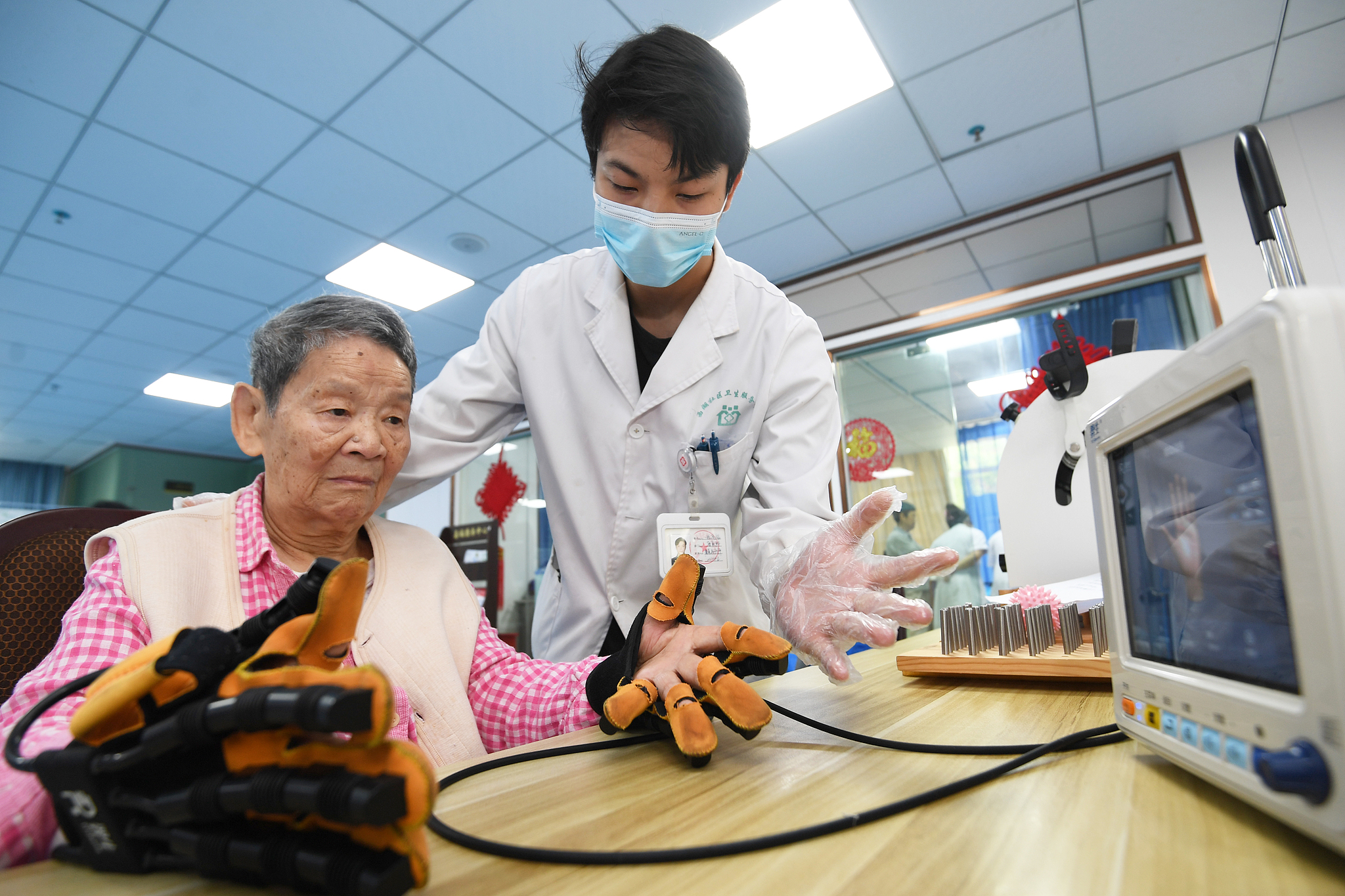 A doctor guides a patient in joint training using pneumatic gloves at the Xihu Community Health Service Center in Nanming District, Guiyang City, southwest China's Guizhou Province, June 13, 2024. /VCG