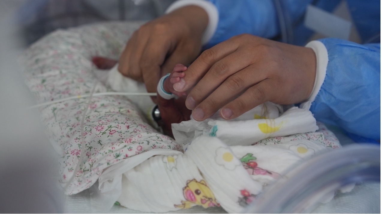 A premature baby in an incubator holds neonatologist Tian Congliang's finger as he listens to her heartbeat in the NICU at Naqu People's Hospital, Xizang Autonomous Region, July 21, 2025. /CGTN