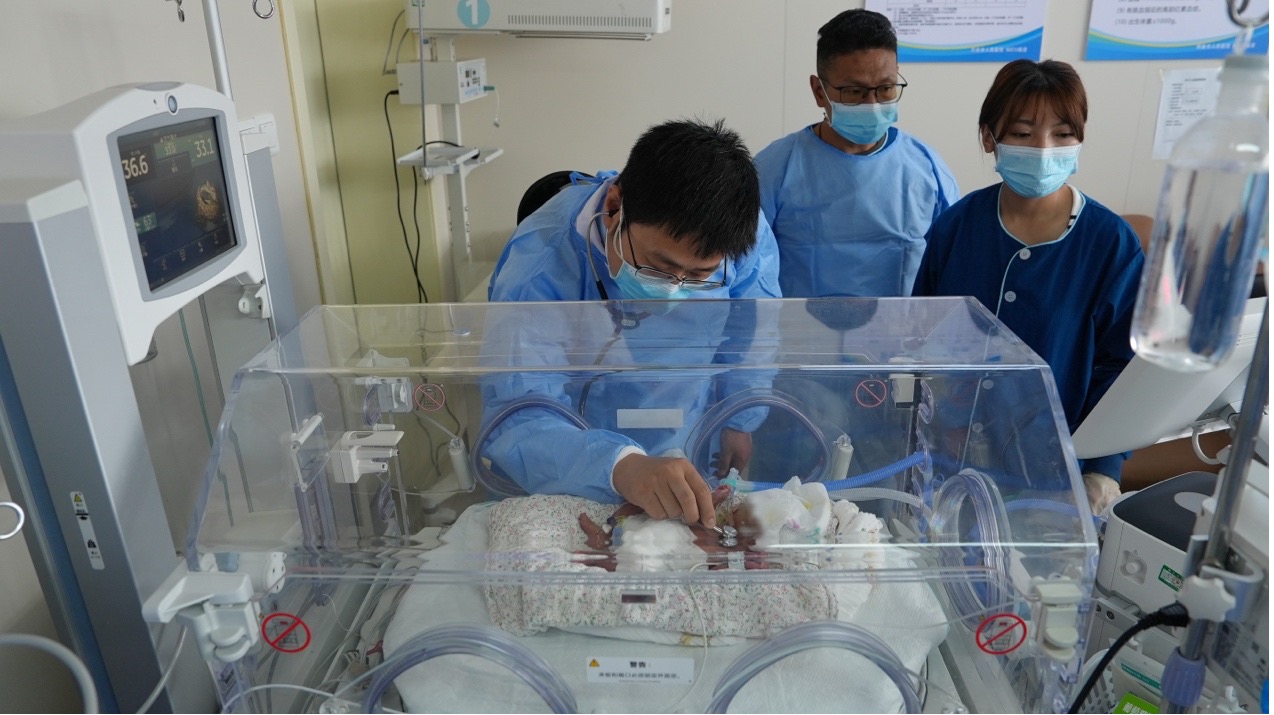 Neonatologist Tian Congliang (left) listens to a premature baby's heartbeat with a stethoscope in the neonatal intensive care unit (NICU) at Naqu People's Hospital, Xizang Autonomous Region, July 21, 2025. /CGTN