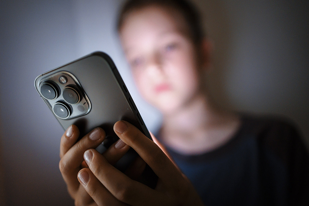 A child looks at a smartphone display in the dark. /CFP