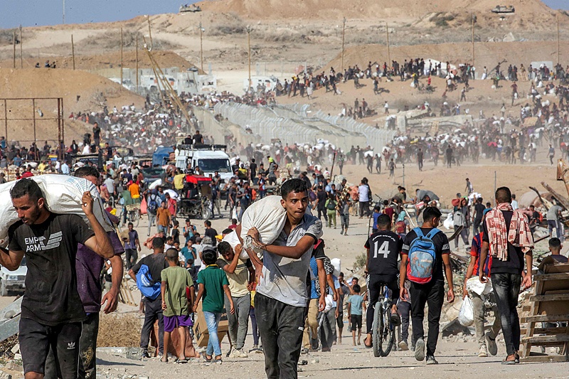 A youth walks with a sack on his shoulder with other people carrying bags of humanitarian aid while the turrets of Israeli army main battle tanks are pictured in the background in the central Gaza Strip, Palestine, August 22, 2025. /VCG