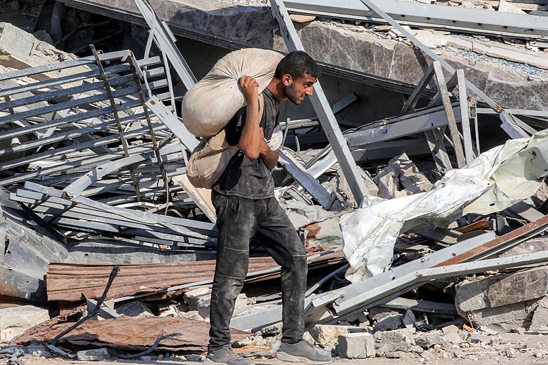 A man carries a sack of humanitarian aid while walking past the rubble of a collapsed building in the central Gaza Strip, Palestine, August 22, 2025. /VCG