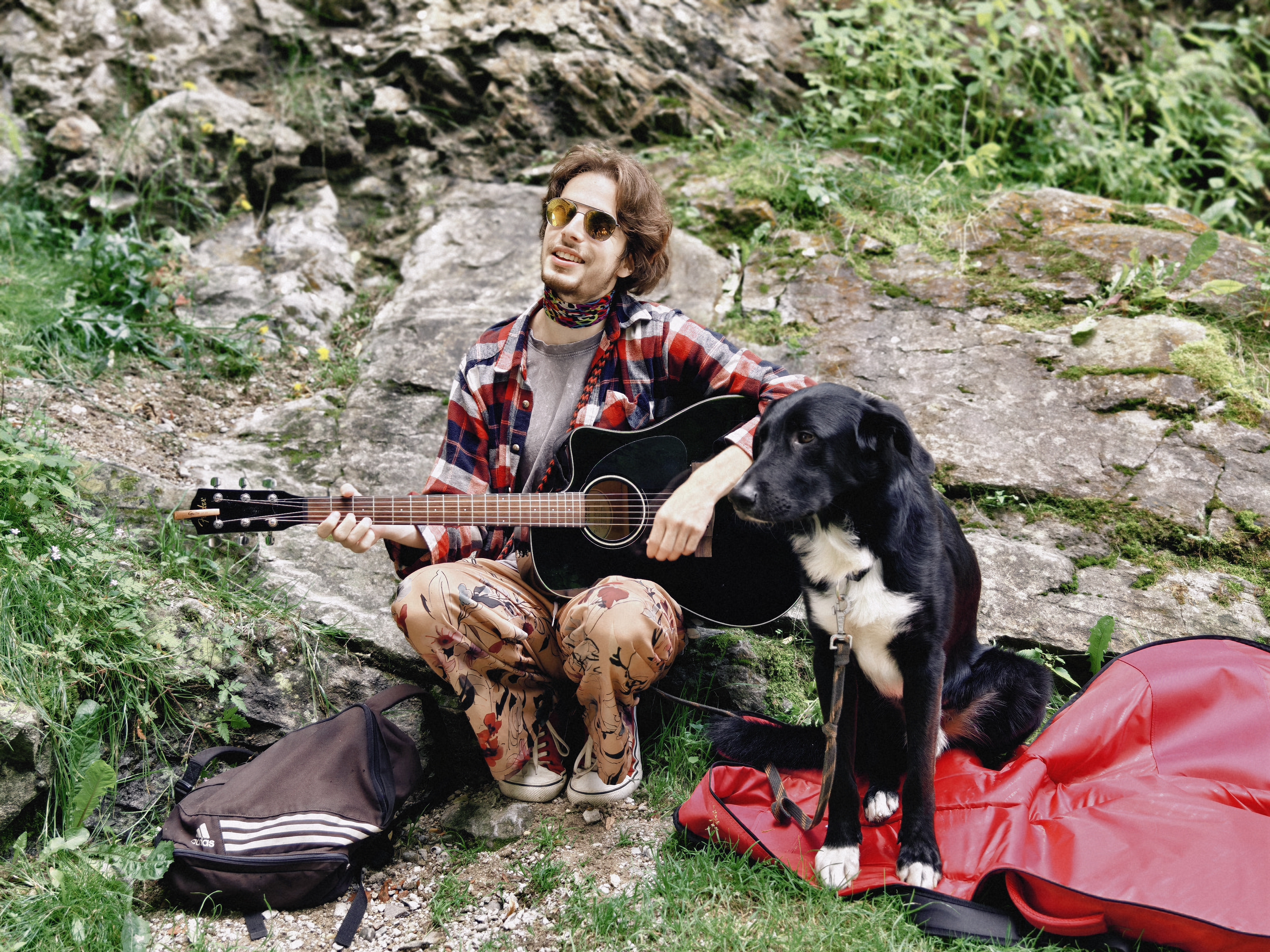 Melodies in the Mountains, a Dog at My Side: With green hills as a backdrop and grass as a seat, a lone figure and a dog sit while a guitar hums softly. Sunlight spills through the cracks in the stones, warming the plaid shirt, as notes drift with the mountain breeze. The black dog rests quietly beside them, turning the freedom of the journey into a lively melody. Every moment spent close to nature is a gentle act of ecological stewardship, reflecting harmony between humans and the environment. Every step leaves no mark on the land, every pause shows respect for all living things, and each strum of the strings reminds us: freedom and contentment are not just fleeting feelings—they can become a sustainable way of life, where humans and nature nourish each other and grow together in shared beauty. /Wang Jingbo