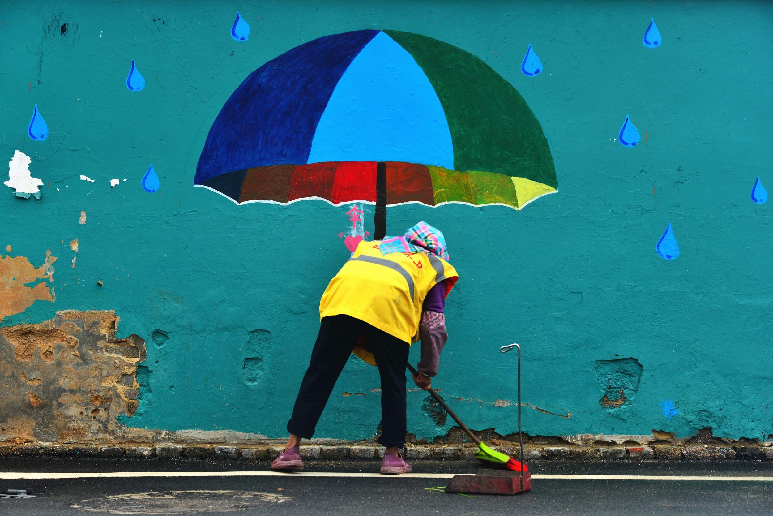Endless Rain: The morning light is faint, and the rain falls like a woven curtain. A sanitation worker braves the rain to sweep the streets, while a large umbrella painted on the wall seems to shelter her from the storm—ordinary acts creating beauty, ordinary lives earning respect. That “umbrella on the wall,” quietly shielding a worker in the rain, is society's gentle and fair tribute to those who give selflessly. The streets in the rain are unusually calm, reflecting the quiet foundation of urban life. Respecting every ordinary contribution is more than courtesy – it is a way of building everyday justice and harmony. Hands that diligently sweep the streets secure livelihoods and dignity, while bringing cleanliness and order to the city. This is a vivid illustration of UN Sustainable Development Goal 8 (Decent Work and Economic Growth): every job deserves respect, every labor deserves appreciation. Such steadfastness aligns with global development initiatives – eradicating poverty and promoting inclusive growth rely on the stability and dedication of countless ordinary roles. It also echoes the ideals of global civilization initiatives, which emphasize mutual respect and understanding; a society that values and honors labor is a truly civilized society. In the steady rain, it is these countless ordinary figures who quietly gather into a force that propels society forward. /Zhang Hongwei