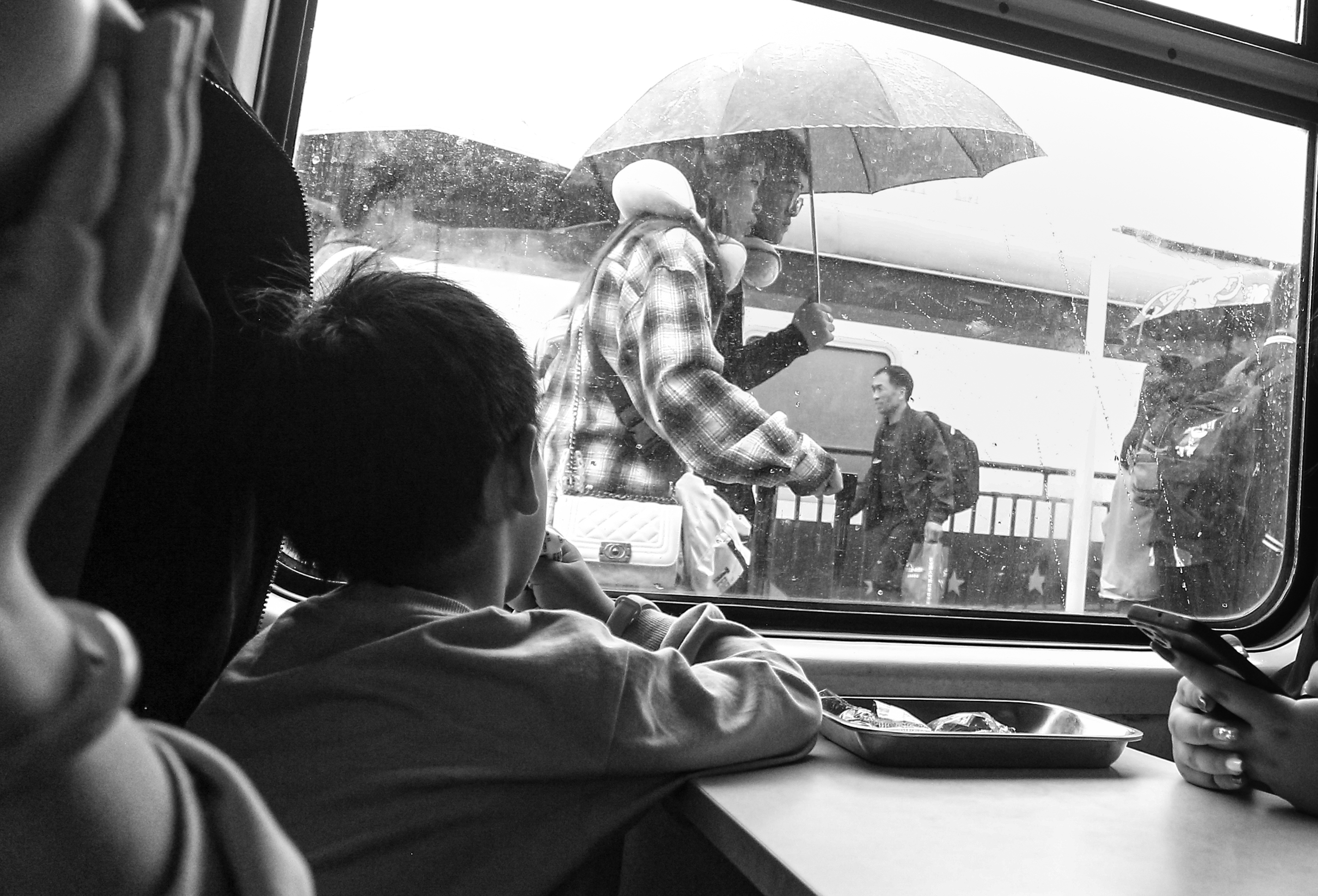 Outside the Window: In the carriage on a rainy day, a little boy lies prone by the window. His eyes are following the pedestrians holding umbrellas outside. Under the umbrella is a young couple snuggling up – a scene of warmth. The raindrops trace their way down the car window, blurring the boundaries like a silent wall. The boy looks on quietly, with the world outside reflected in his innocent eyes. It seems as if he is counting the raindrops or perhaps imagining the warmth under the umbrella. Outside the car, people come and go while he is inside with a hazy gaze framed by the car window. In this new era of social development, everything is so warm and beautiful. Perhaps he doesn't understand yet that this warmth is the epitome of a society that promotes mutual assistance and development – a safe and orderly environment and a world that respects diverse civilizations. And this world is exactly what people strive for together. Every bit of fairness and care is accumulating strength for sustainable cities and communities, making harmony and warmth between humans and the environment, as well as among people, the true sustainable cornerstone of society. /Wang Bohao