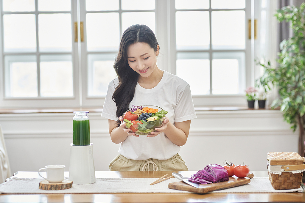 Una mujer joven que sostiene un tazón de coloridas frutas y verduras. /VCG