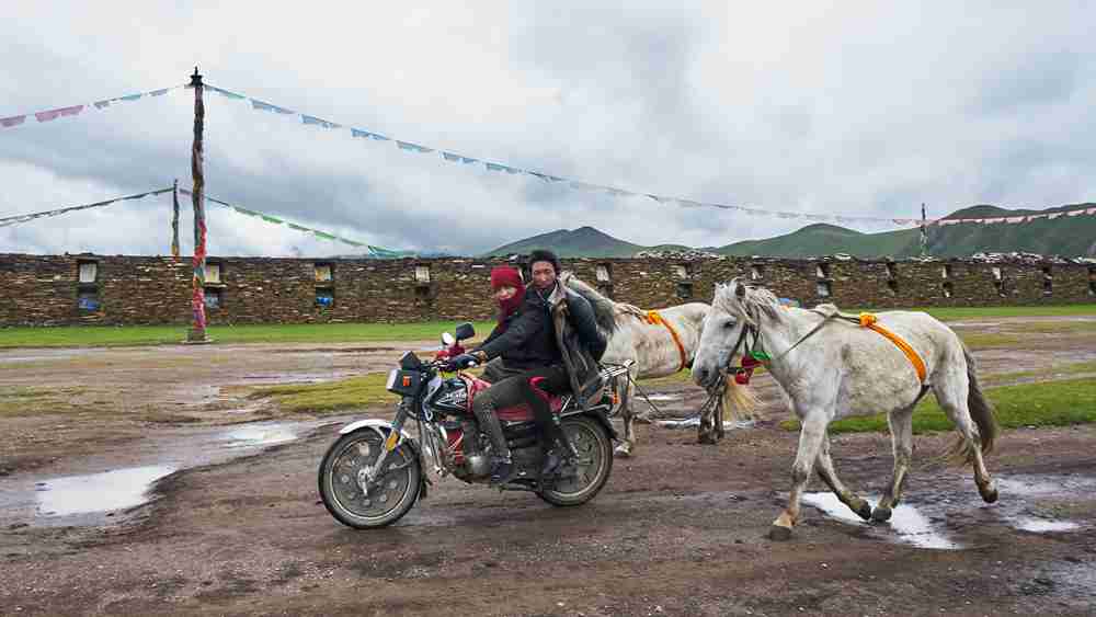 By the world's longest Bage Mani Wall, on a wet muddy road after rain, two Tibetans ride a motorcycle, with a white horse trailing slowly behind, its orange bridle straps fluttering. The Mani Stone Wall and prayer flags, under the overcast sky, silently guard the ancient faith.
This scene embodies the warmth of the UN Sustainable Development Goal of 
