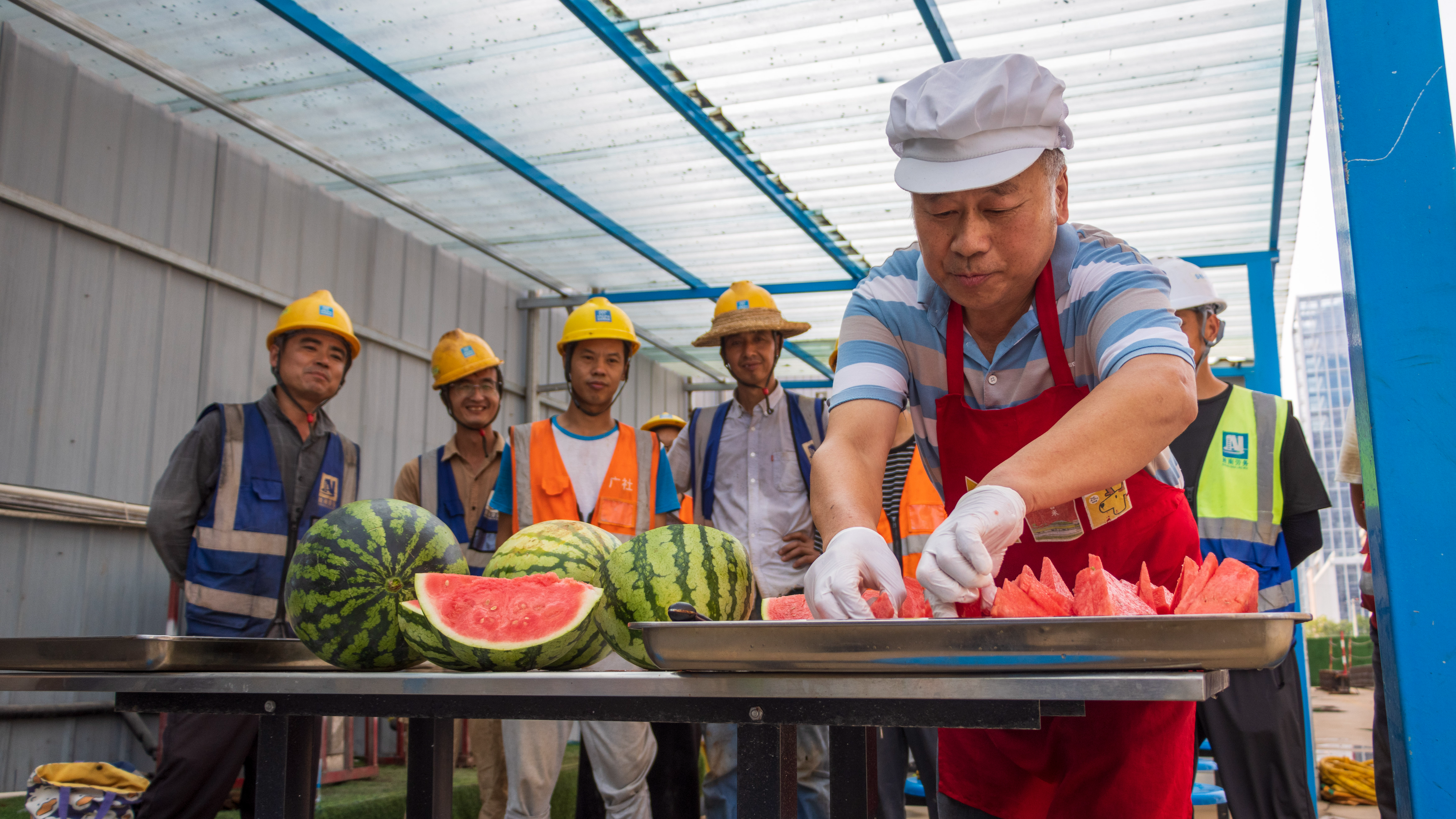 On a construction site, beneath a translucent sunshade, chef hats and safety helmets come together. Slices of watermelon are passed from hand to hand – to steelworkers, carpenters and managers alike – all savoring the same sweet refreshment. This moment reflects the United Nations Sustainable Development Goal of 