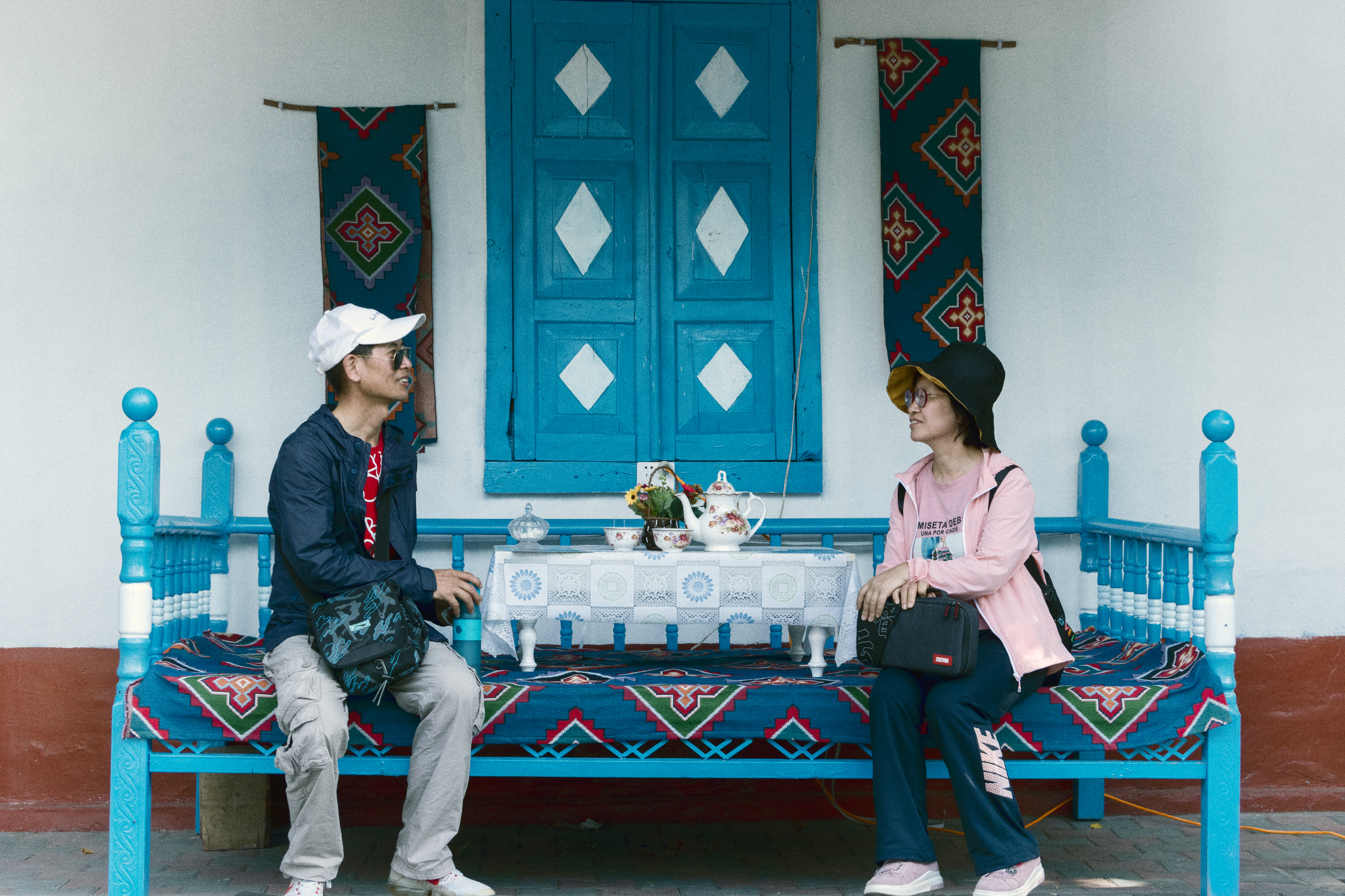 Dialogue in Kazanqi: In Kazanqi Town, Xinjiang, between blue-hued walls and a cobalt-colored couch, a couple sits face-to-face, chatting quietly about daily life. Tea sets are serenely arranged on the table, accompanied by distinctive ethnic-styled patterns.
This scene aligns with the UN Sustainable Development Goal of 