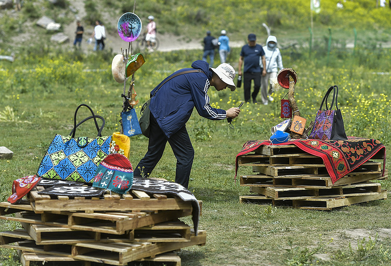 A tourist takes photos of Kazakh embroidery in a park in Urumqi, the capital of northwest China's Xinjiang Uygur Autonomous Region, June 15, 2024. /VCG