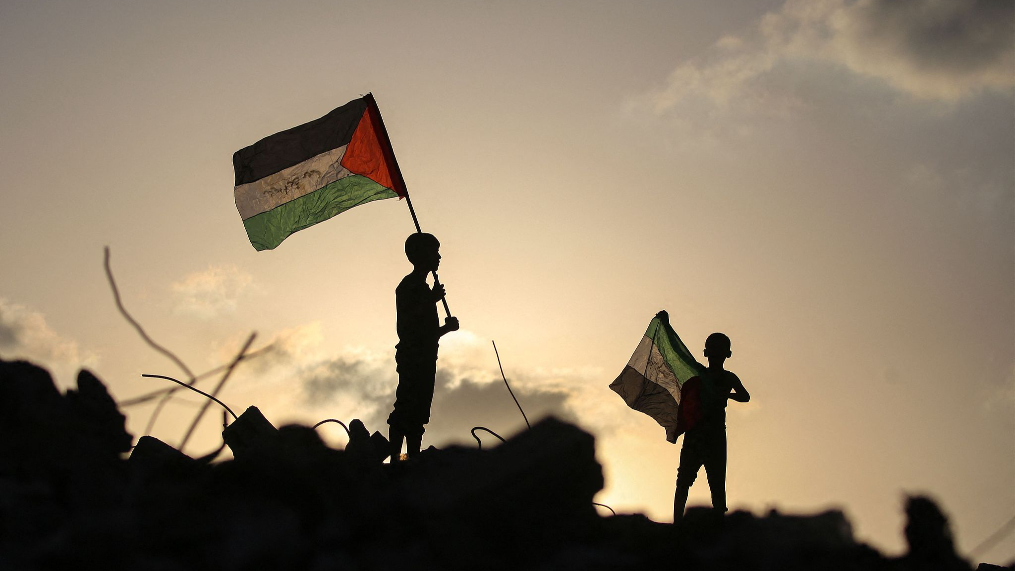 Displaced Palestinian children wave Palestinian national flags as they stand on the rubble of a destroyed building at the Bureij camp for refugees in  central Gaza, September 22, 2025. /VCG