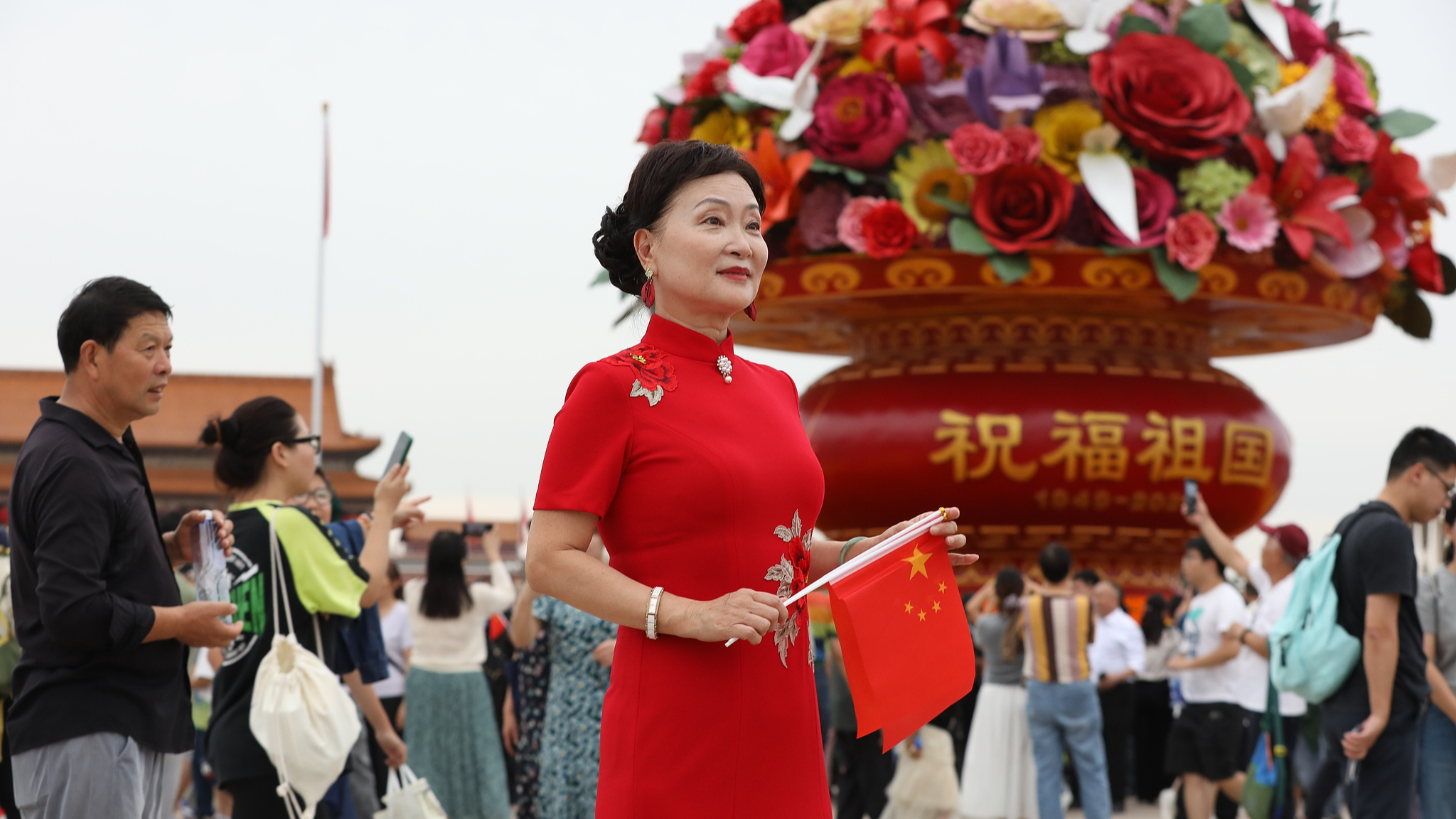 A woman carrying national flags stands next to a flower basket, Beijing, China, October 1, 2025. /VCG