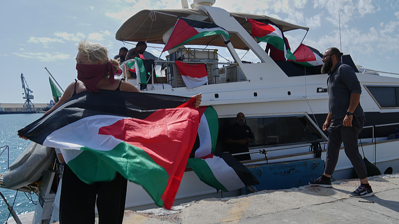 An activist holds a Palestinian flag in front of a boat of the civilian, Gaza-bound Global Sumud Flotilla as it is docked at the port in Larnaca, Cyprus, October 3, 2025. /VCG