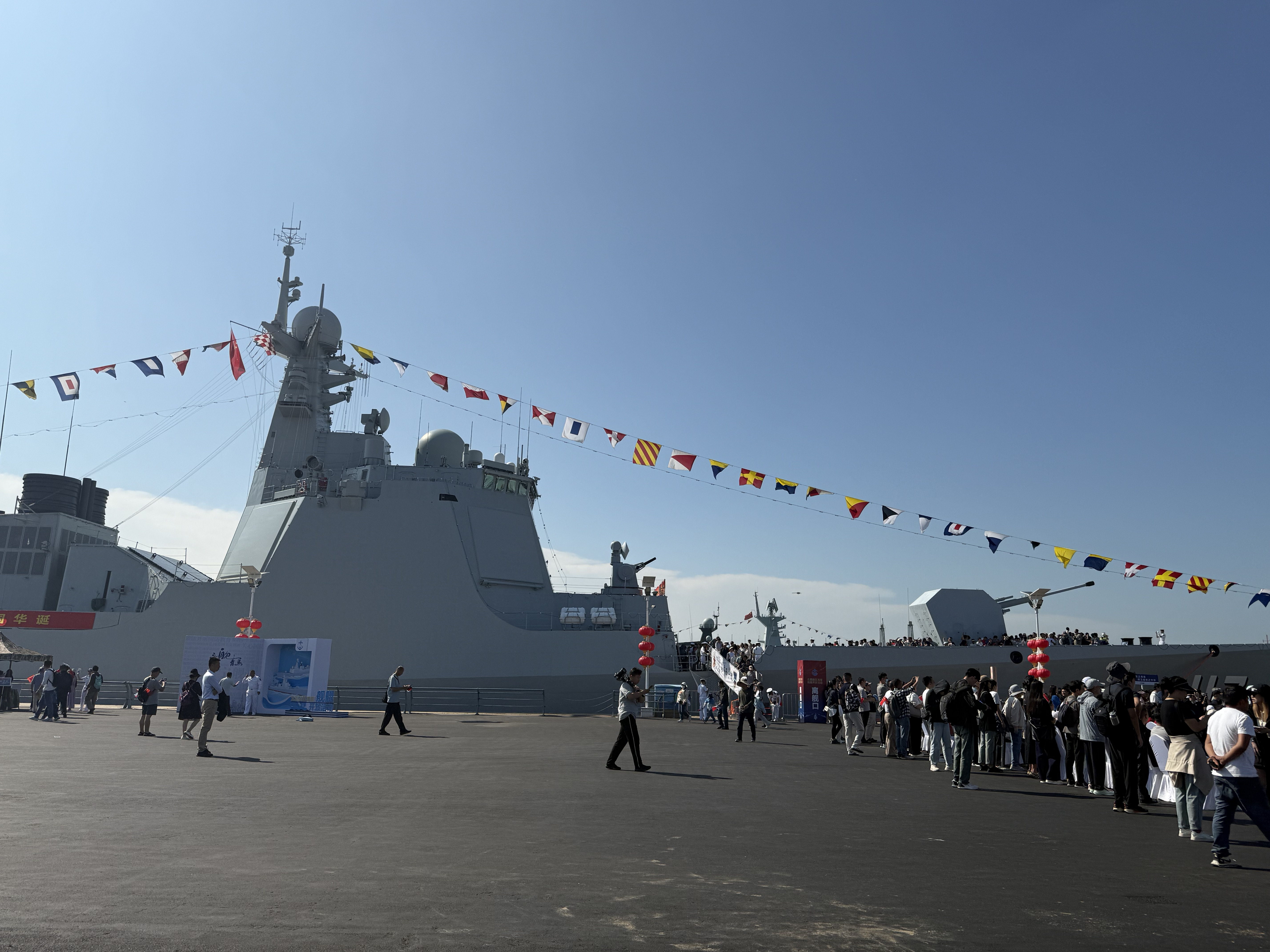 Festival celebrations unfolding along the waterfront promenade against the backdrop of a large naval vessel, September 2025, Qingdao, China /Zaruhi Poghosyan