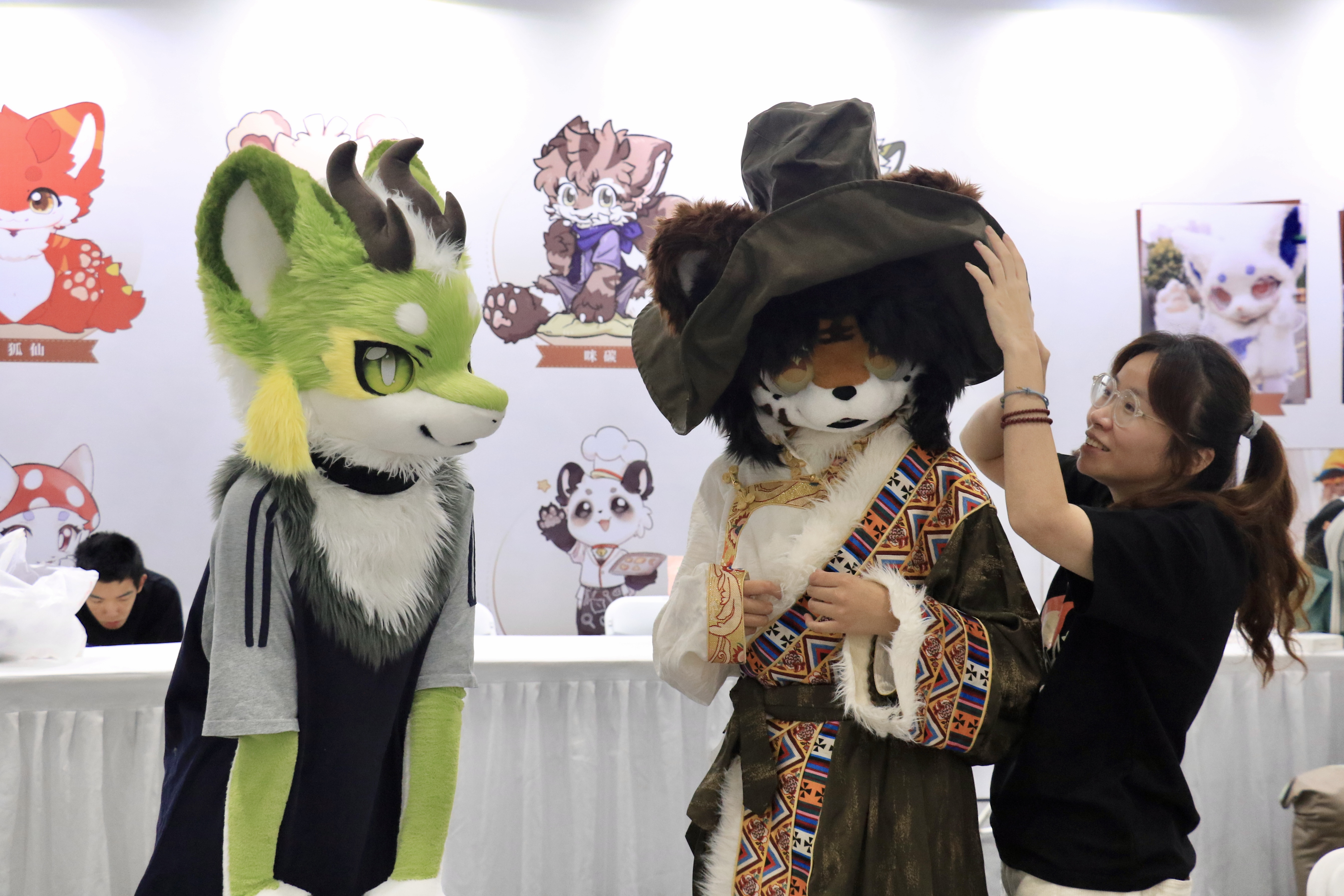 A woman helps a fursuit cosplayer adjust their headpiece (fursuit refers to a full-body, animal-themed costume worn by members of the furry fandom) at the International Anime Goods Festival (IAGF) at Hangzhou City, east China's Zhejiang province, October 2, 2025. /CFP