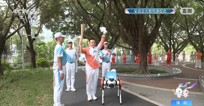 A robot dog hands the mascots to a torchbearer. /CMG