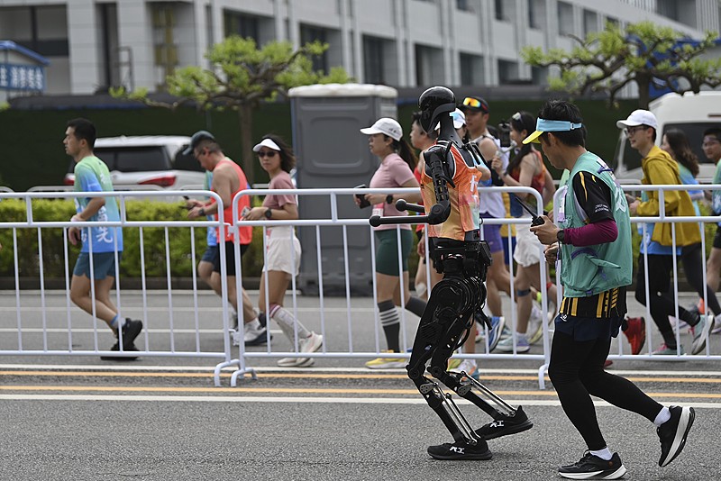A robot runs alongside humans at the Beijing Yizhuang Half Marathon and Humanoid Robot Half Marathon in Beijing, April 19, 2025./VCG
