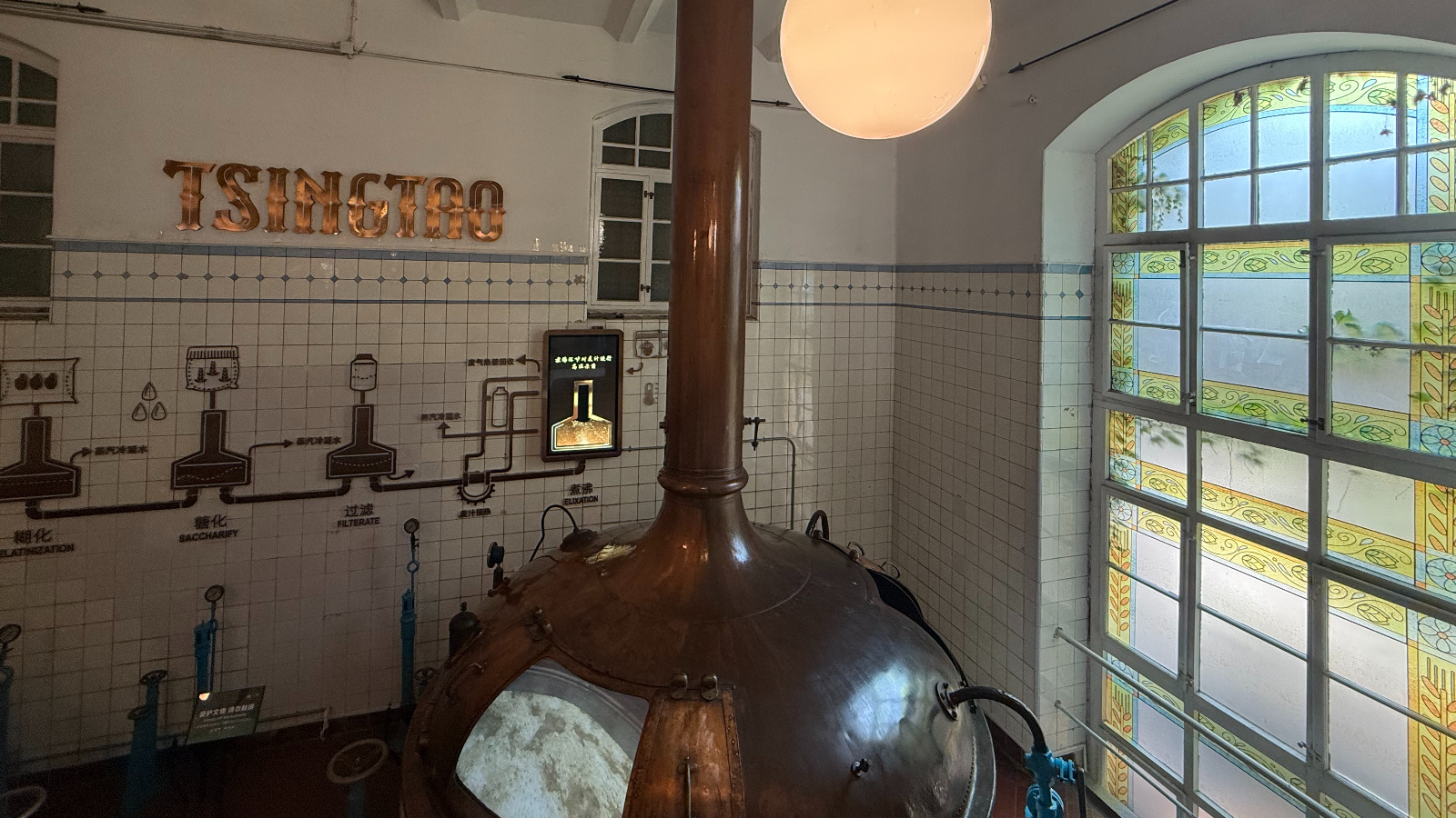 A gleaming copper brewing cauldron catches the light beneath the Tsingtao Beer Museum's stained glass window, Qingdao, September 2025, Zaruhi Poghosyan. /CGTN