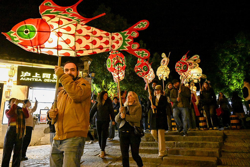 International visitors join a fish lantern performance, an intangible cultural heritage activity, in Hongcun Scenic Area in Yixian County of Huangshan, Anhui on November 15, 2025. /VCG
